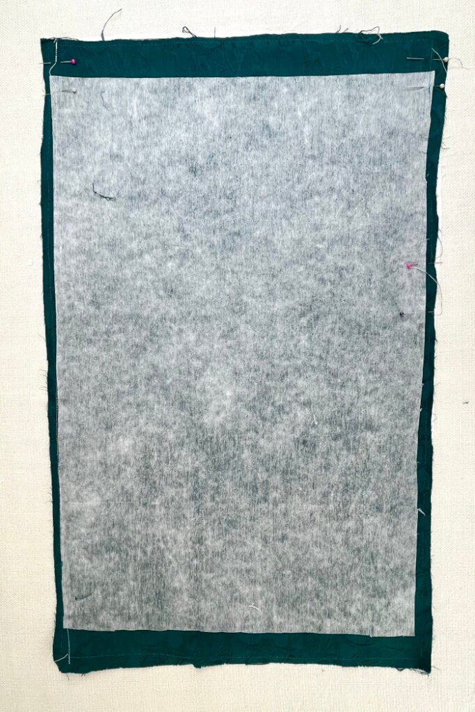 Backing fabric, lining fabric and interfacing sewn together with pins indicating turning holes for the advent calendar base panel.