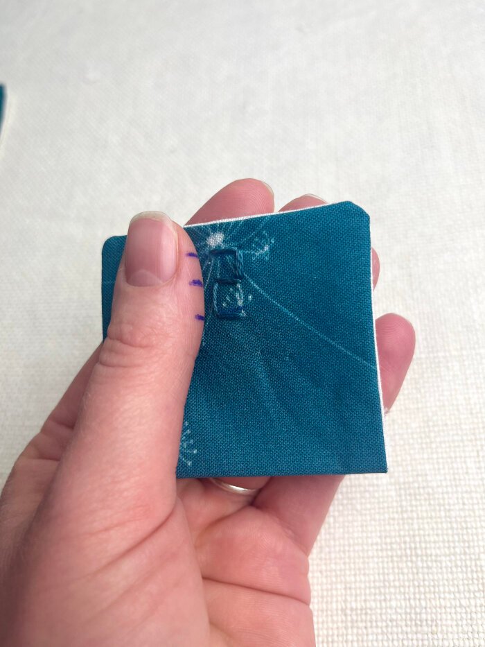 Hand-embroidered advent calendar numbers stitched onto fabric pockets using complimentary embroidery thread. Simple decorative detail.