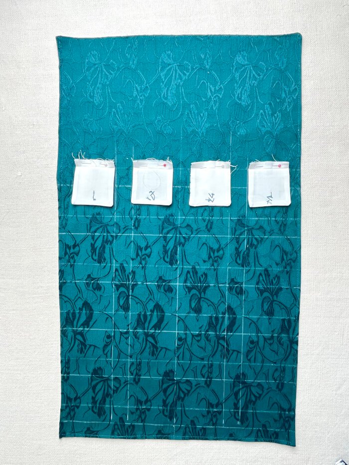 Fabric pockets arranged on the advent calendar backing panel to plan spacing and layout before sewing.