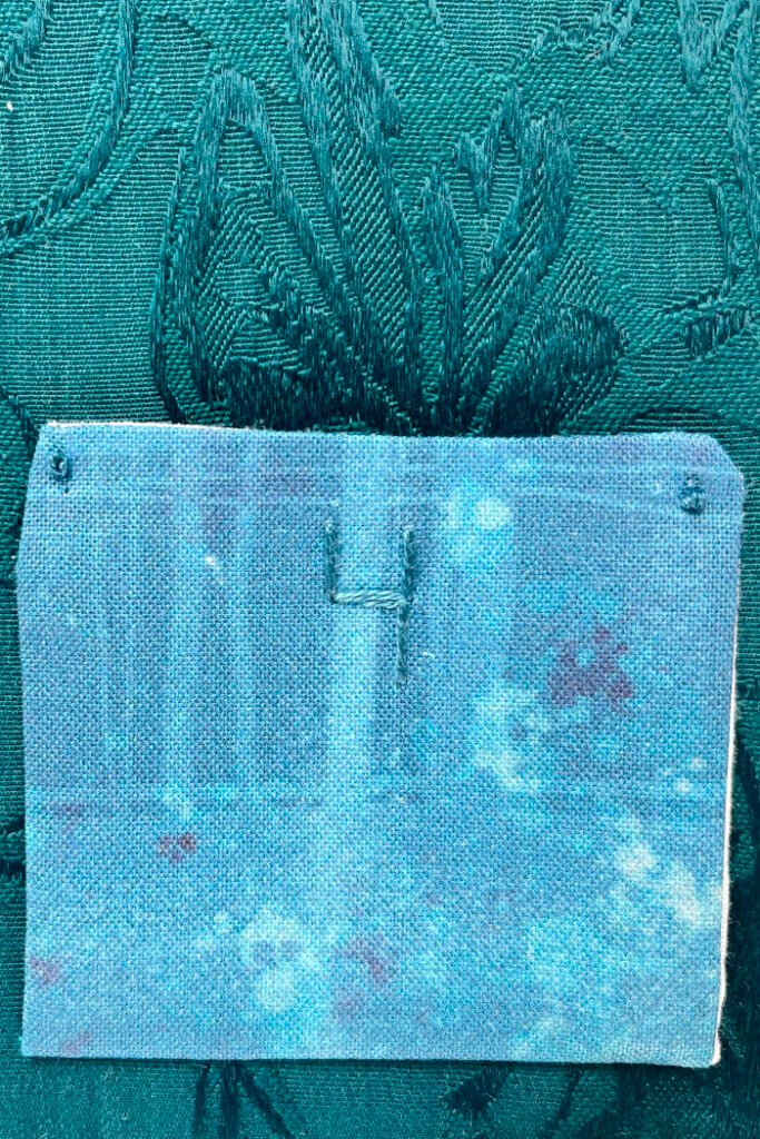 Pressed pockets folded upward with corners tacked in place using decorative embroidery stitches on a handmade advent calendar.