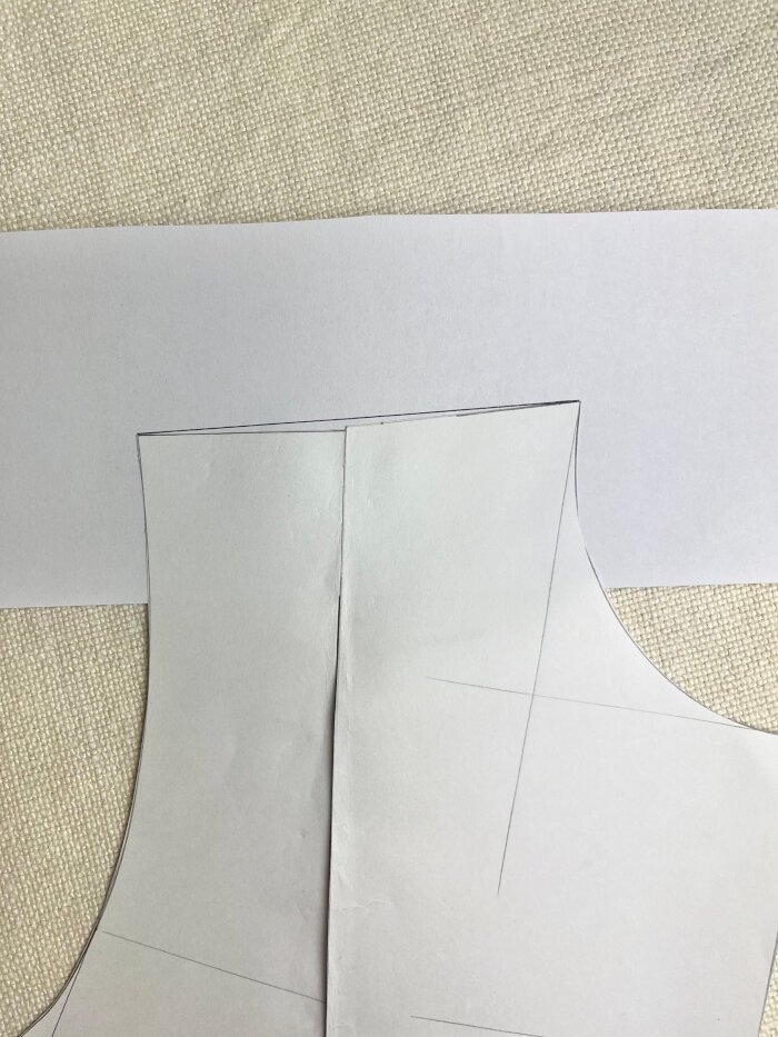 Correcting a dipped shoulder seam on the bodice block by gluing the pattern to paper and redrawing a smooth shoulder line.