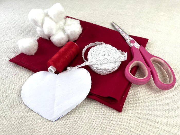 Materials needed to sew a heart shaped fabric brooch including cotton fabric, lace trim, stuffing and thread