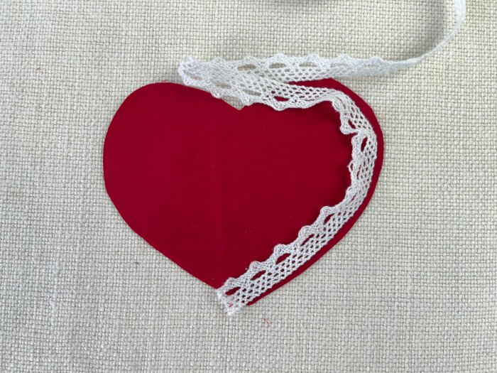 Placing lace trim along the edge of a heart shaped fabric piece before sewing