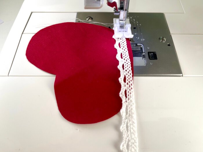 Sewing lace trim around the curved edges of a heart shaped fabric piece