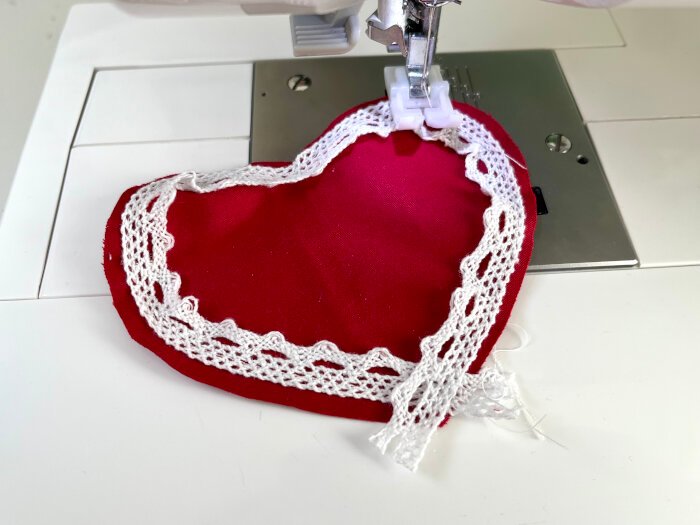 Sewing lace trim around the curved edges of a heart shaped fabric piece