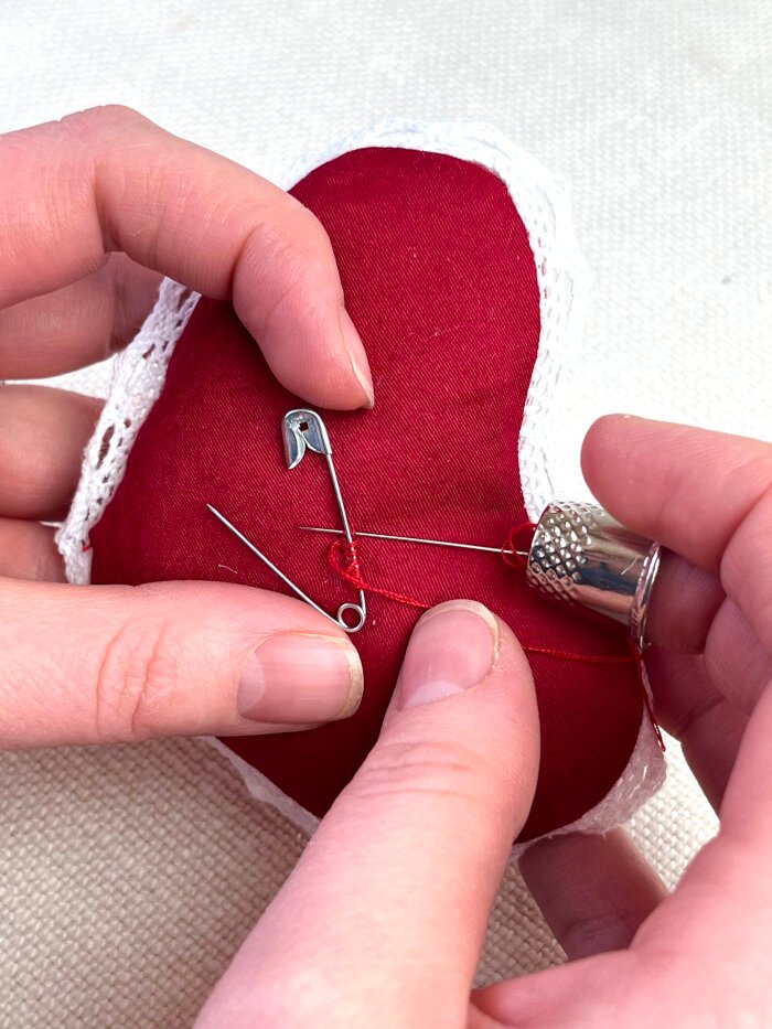 Hand sewing a safety pin onto the back of a heart shaped fabric brooch