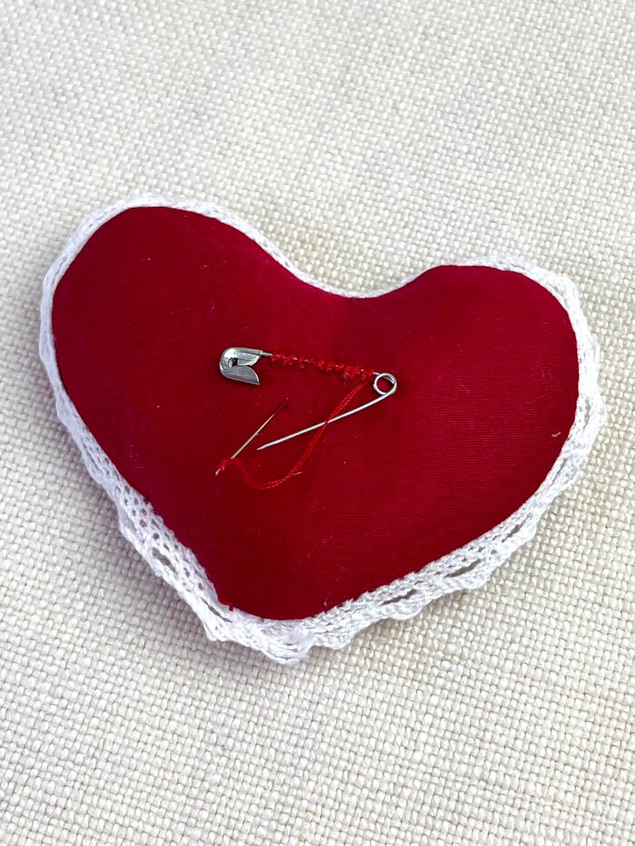 Hand sewing a safety pin onto the back of a heart shaped fabric brooch