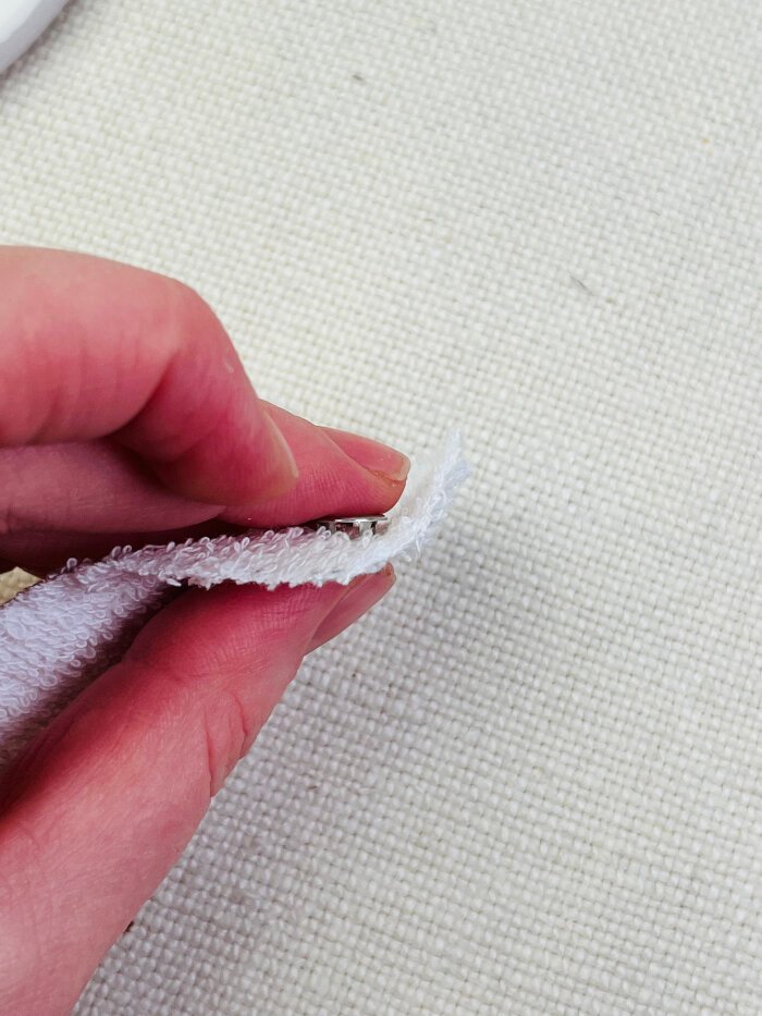 Metal snap button cap with prongs pushed evenly through fabric before setting the snap without pliers
