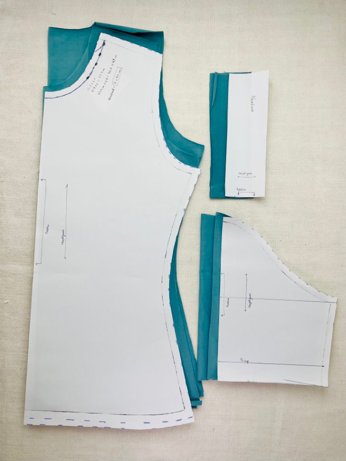All fitted T-shirt pattern pieces cut from jersey fabric with paper bodice, sleeve, and neckband patterns placed on top for a women’s custom T-shirt sewing project