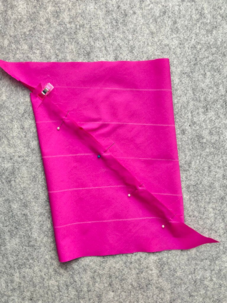 How to Make Bias Binding (Step-by-Step Tutorial for Beginners) Matching marked lines and pinning fabric edges to form tube for continuous bias binding.