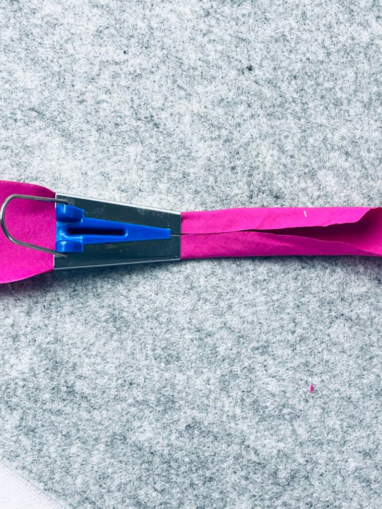 How to Make Bias Binding (Step-by-Step Tutorial for Beginners) Feeding fabric strip through bias tape maker tool before pressing to create even bias tape.