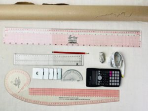 Flat lay of essential sewing pattern drafting tools including grading ruler, French curve, pencil and pattern paper