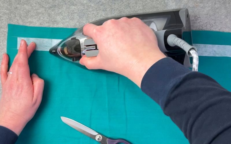 Applying fusible interfacing to button stand area with hot steam iron on wrong side of fabric