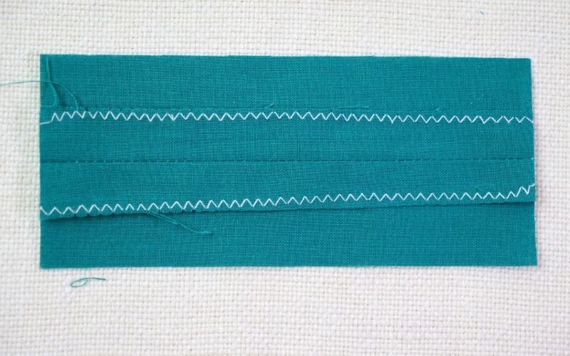Different Types of Seam Finishes That Look Professional A close-up photograph of a fabric edge secured with a zigzag stitch finish, showing how the sewing machine stitch wraps over the raw edge to stabilize it and prevent unravelling.