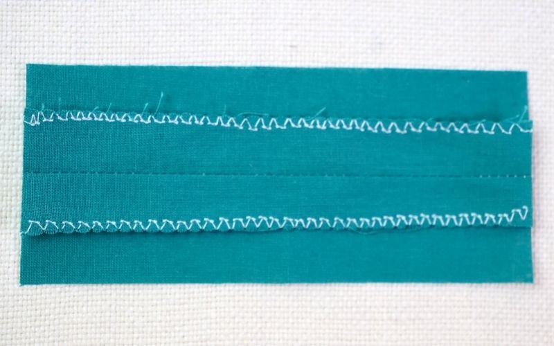 Different Types of Seam Finishes That Look Professional An image illustrating an overedge stitch applied to a fabric edge on a regular sewing machine, highlighting the dense, securing stitch that prevents fraying and tunneling without an overlocker